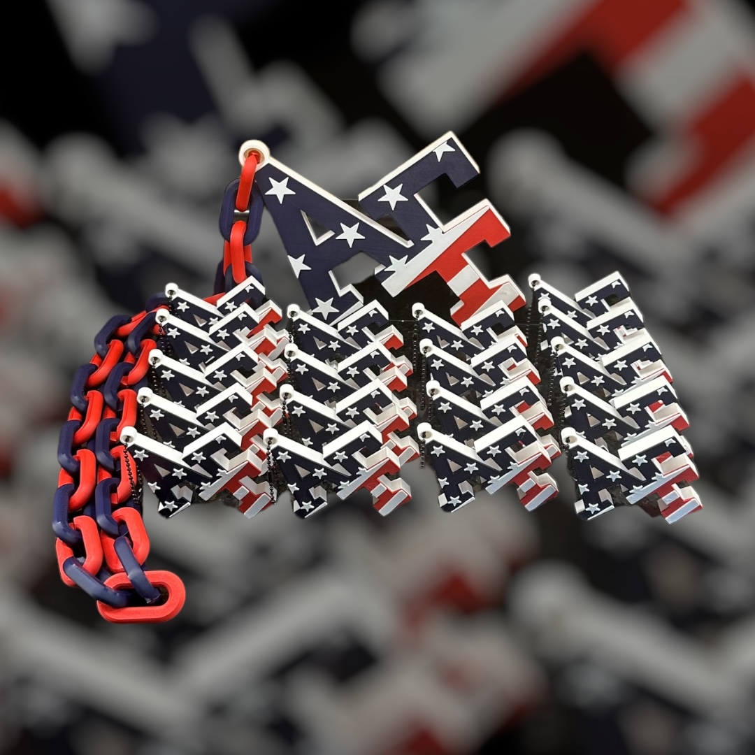 A finished red, white and blue 10×10 chain necklace with pendant behind a group of matching 2×2 keychains